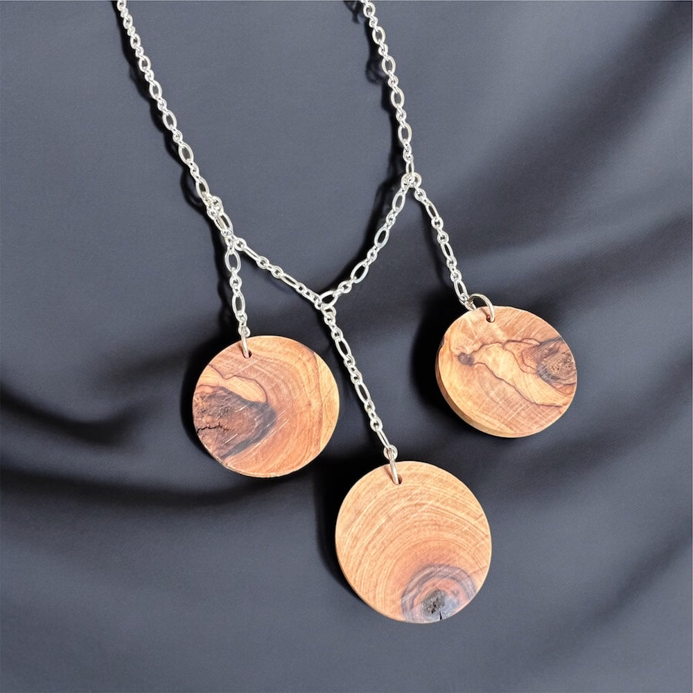 Three olive wood disks hang from a sterling silver plated chain on a black silk background