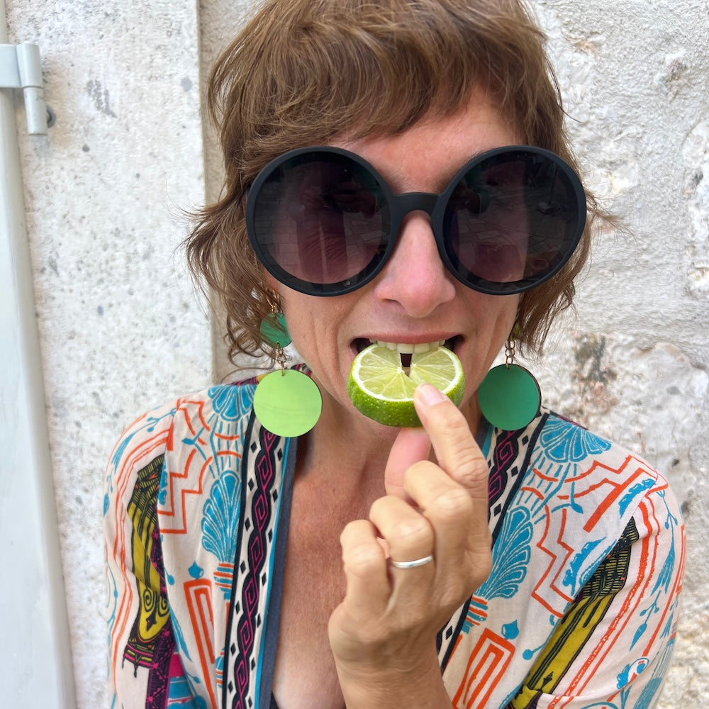 Person wearing sunglasses and colorful clothing, holding a lime to their mouth.