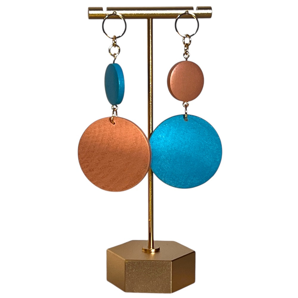 Hand Painted earrings one small circle holds another bigger circle missmatched blue and orange hanging from a stand