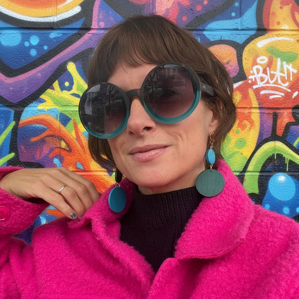 Person wearing a bright pink coat and large blue sunglasses indoors.