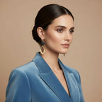 A pair of gold and brass earrings with a black wooden bead hang from a golden earring display. 