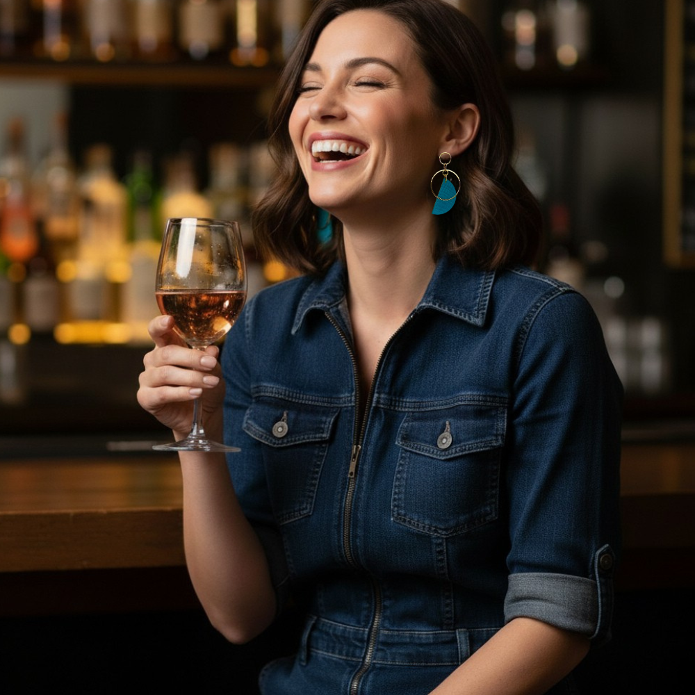 Woman wearing deep teal hand painted half tone earrings, with wine at a bar