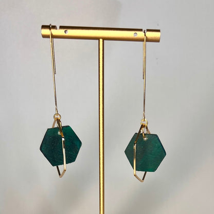 Hand painted wild seas blue- green hexagon wood bead hangs from a rigid gold threader earring - hanging from an earring display. Handcrafted by Madera Design Studio 