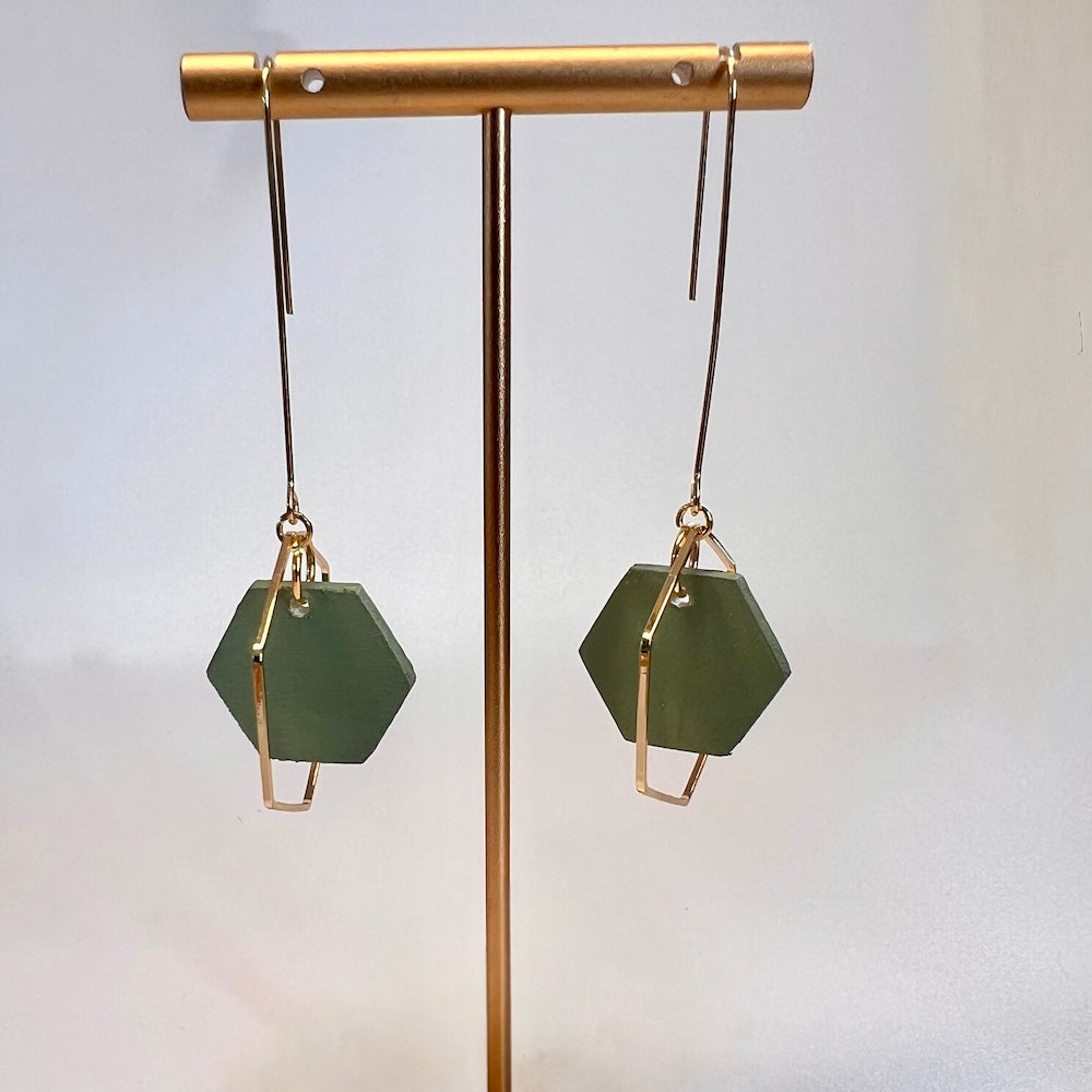 Hand painted forest green hexagon wood bead hangs from a rigid gold threader earring - hanging from an earring display. Handcrafted by Madera Design Studio 