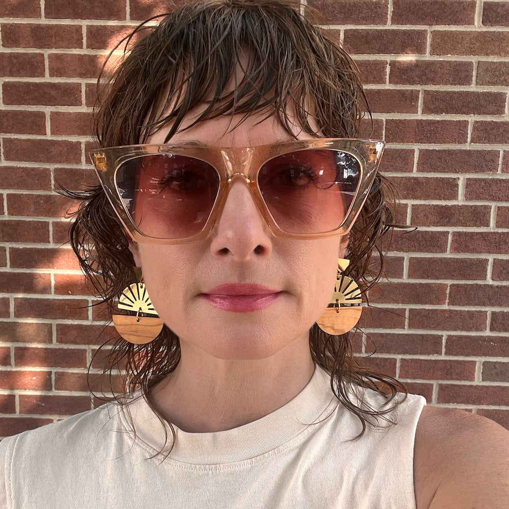 Model wearing Golden Hour Earrings Brass and Olive Wood standing in front of brick wall.
