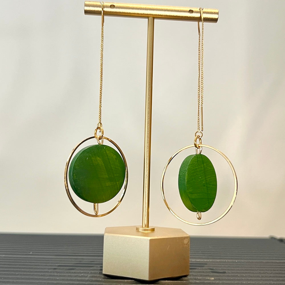 Green painted earrings on a gold stand with a neutral background