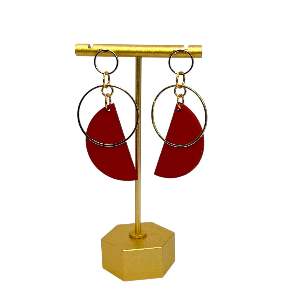 Deep orange earrings with gold hoops on a gold stand against a white background