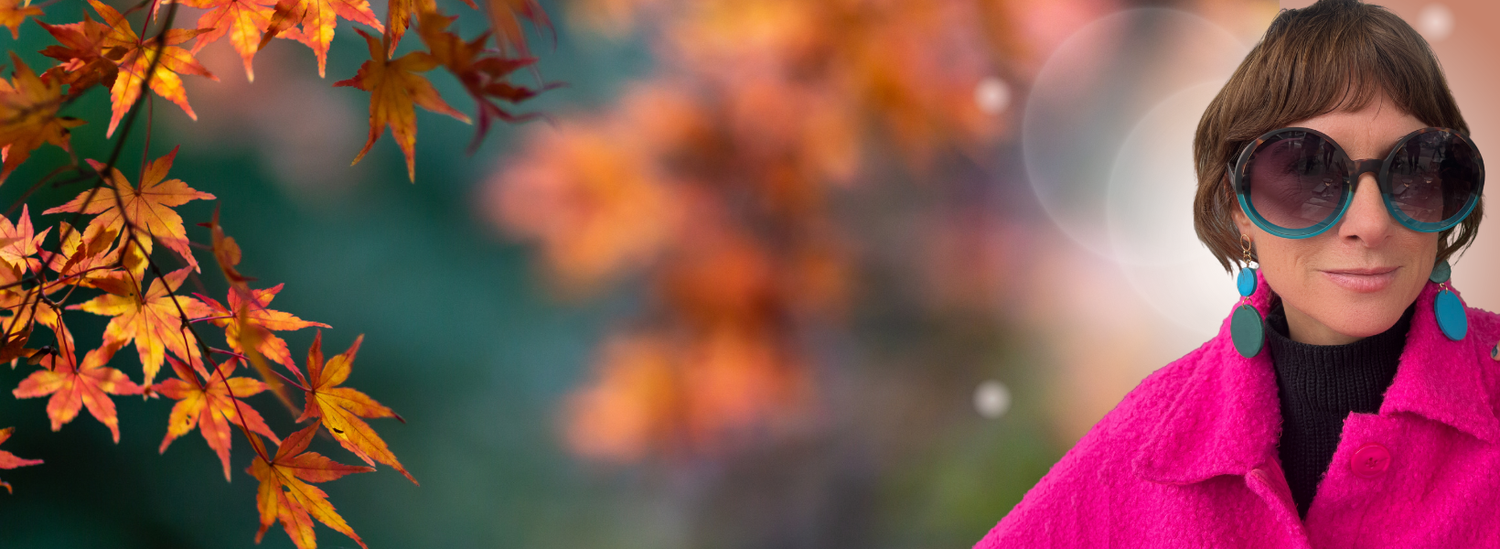 Person wearing sunglasses and a bright pink coat with Mad Era Color Clash Earrings in front of autumn leaves in the background