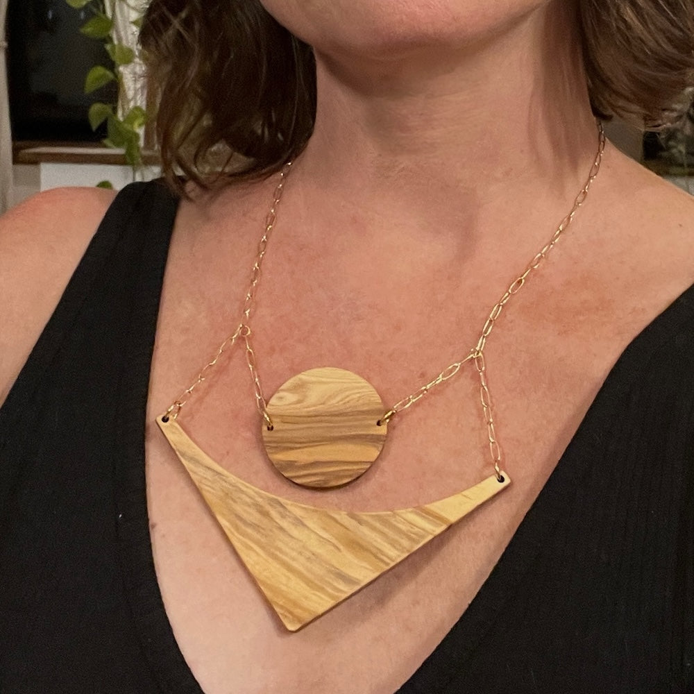 Olive wood circle and triangle pieces hang over each other on a gold chain, on designer Stacey Shevlin - Image links to moon and arrow necklace 