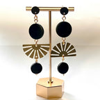 Gold and black earrings on a gold display stand against a white background