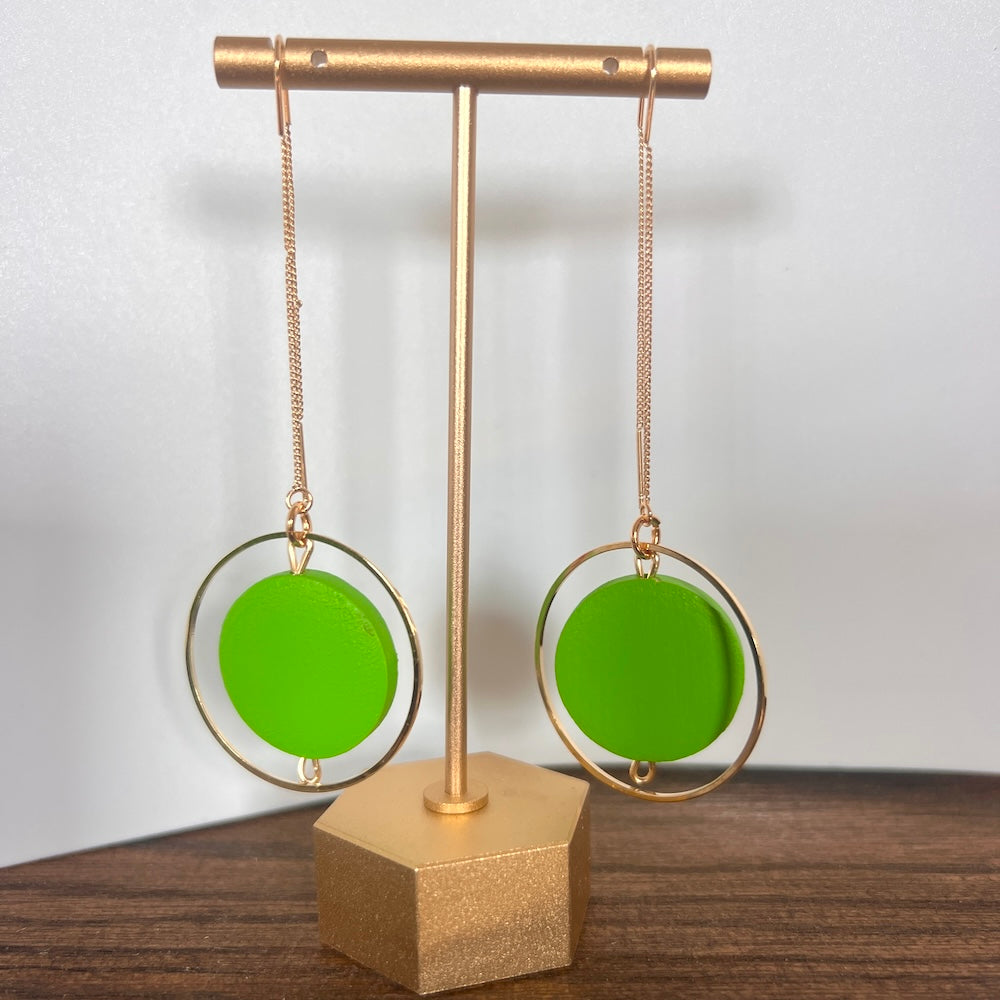 Hand painted Wasabi green hexagon wood bead hangs from a rigid gold threader earring - hanging from an earring display. Handcrafted by Madera Design Studio 