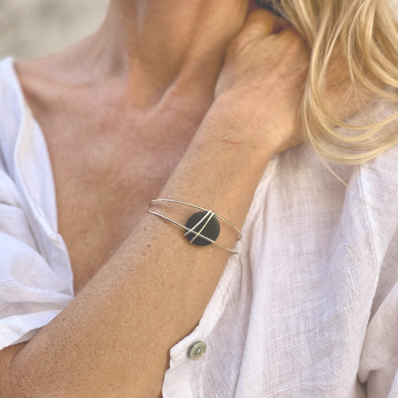 Wooden statement jewelry - close up of a blond woman in a white shirt with her hang across her chest wearing a gold cuff bracelet with a black wood bead handcrafted by Madera Design Studio