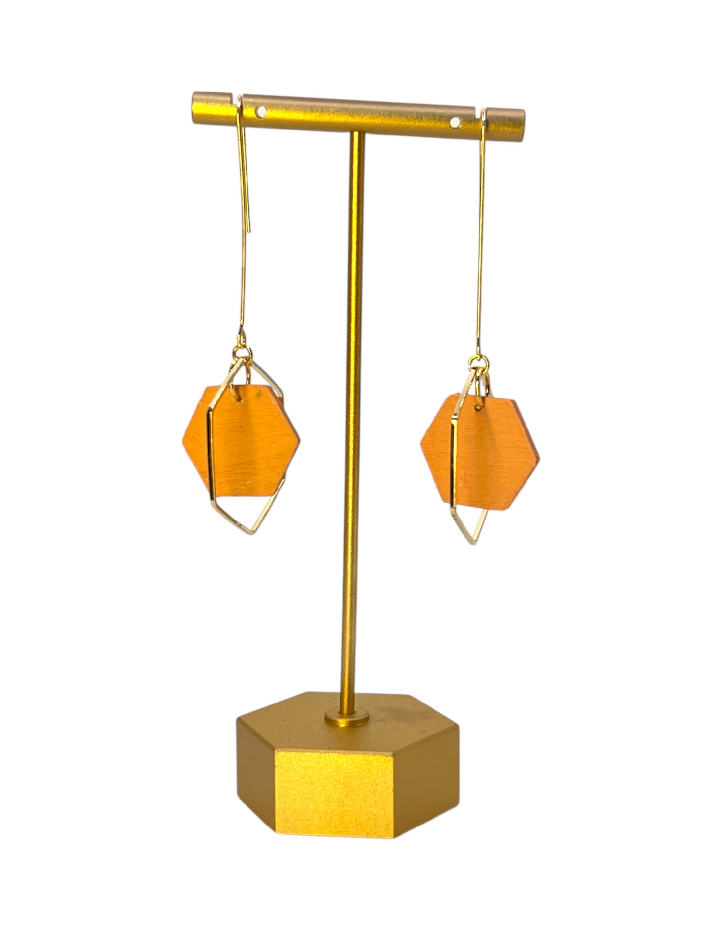 Gold earring stand with two orange geometric earrings on a white background
