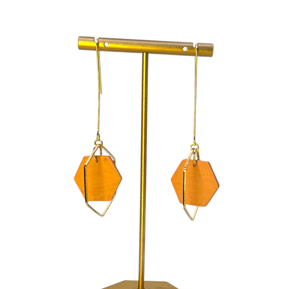 Gold earring stand with two orange geometric earrings on a white background