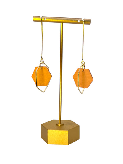 Gold earring stand with two orange geometric earrings on a white background