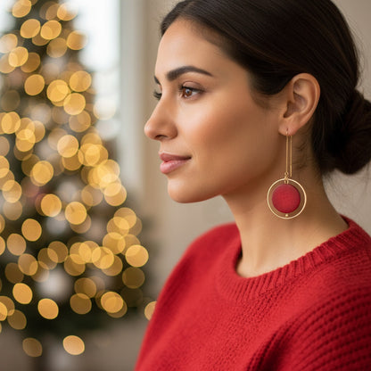 Woman wearing a red sweater and red earrings with a blurred Christmas tree in the background
