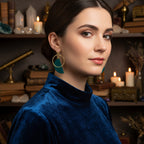 Gold earring stand with green earrings on a white background