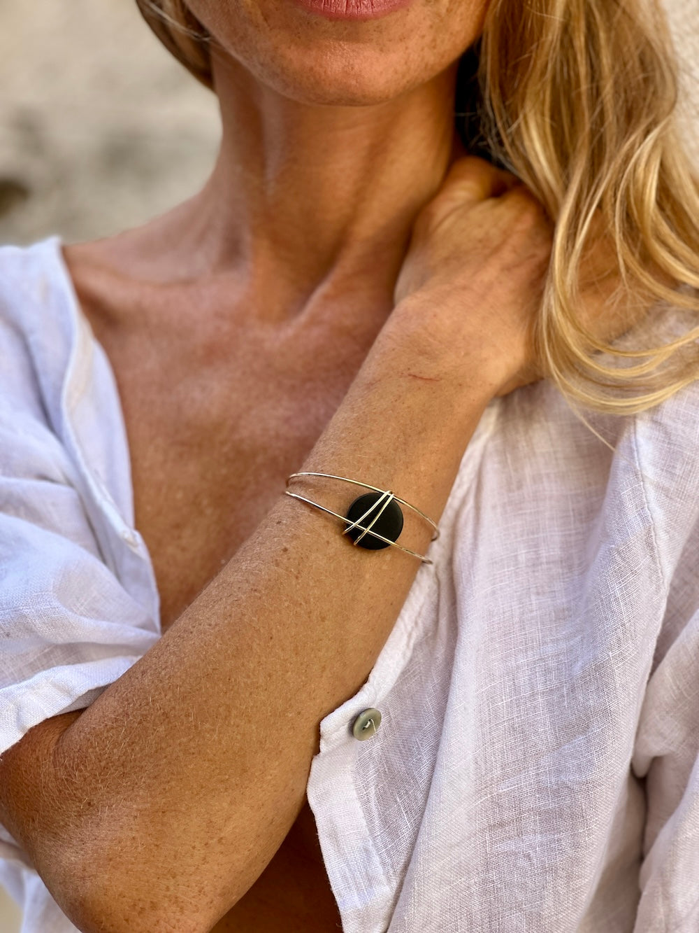 Blond model wearing Madera Design Studio's gold cuff bracelet wtih a black bead