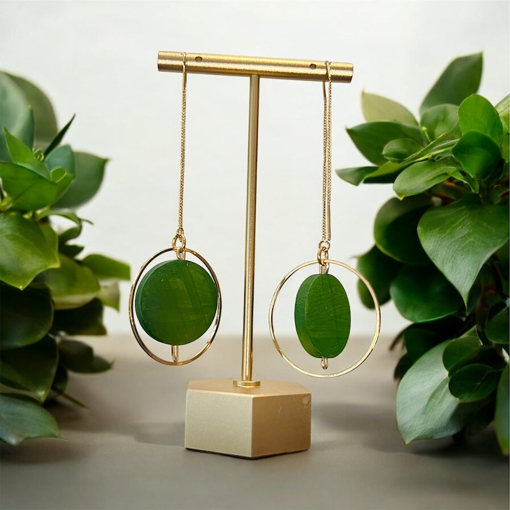 Green earrings on a gold and beige stand with green leaves in the background