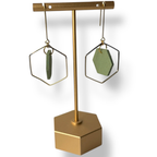Gold hexagonal earring stand with green hand painted earrings on a white background