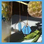 Sky Blue handpainted wooden hexagon beads hang inside a gold plated hexagon , they dangle from a rigid threader earring, and are hanging from a flower in this photo. Handcrafted by Madera Design Studio