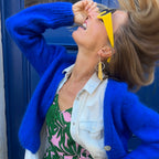 Woman wearing yellow sunglasses and a yellow earring in front of a blue door
