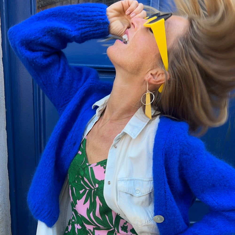 Woman wearing yellow sunglasses and a yellow earring in front of a blue door