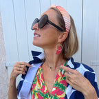 Woman wearing sunglasses, a colorful top, and a headband with a white background
