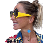 Woman wearing a colorful patterned shirt and yellow sunglasses with a blue earring.