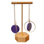 Gold and purple earrings on a gold stand against a light background