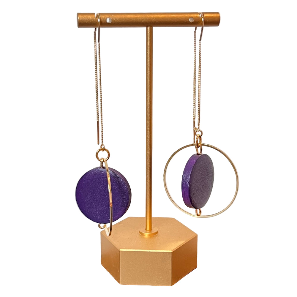Gold and purple earrings on a gold stand against a light background