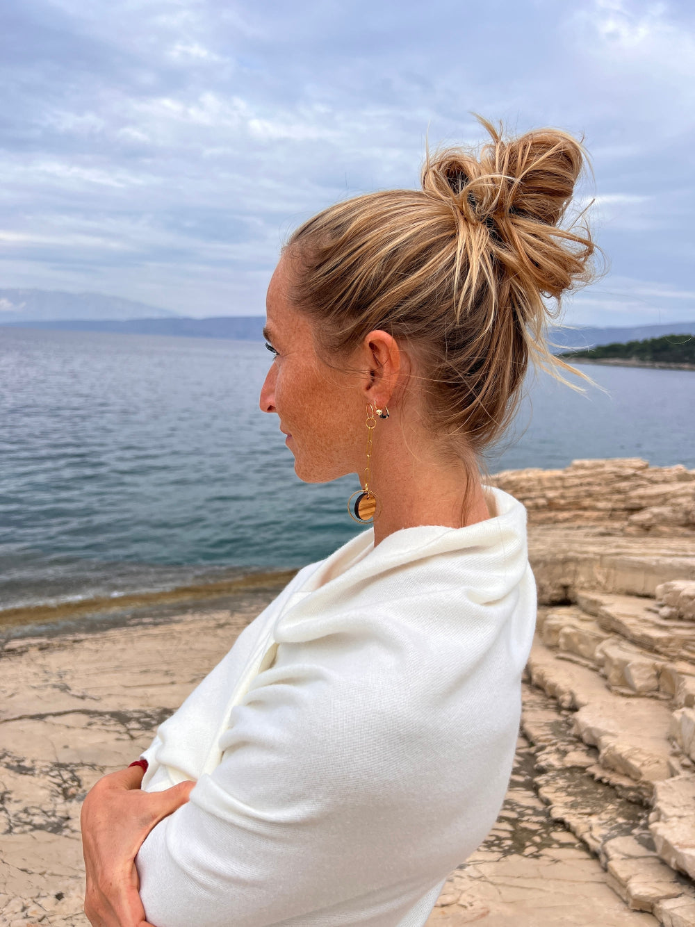 Woman staring at the sea in a white scarf, wearing olive wood and gold chain link earrings by Madera Design Studio - image links to olive wood jewelry collection