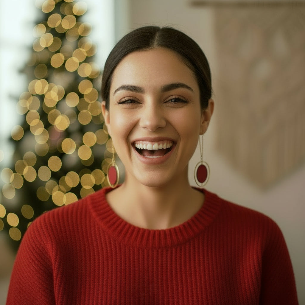 Woman wearing a red sweater and large earrings with a blurred Christmas tree in the background